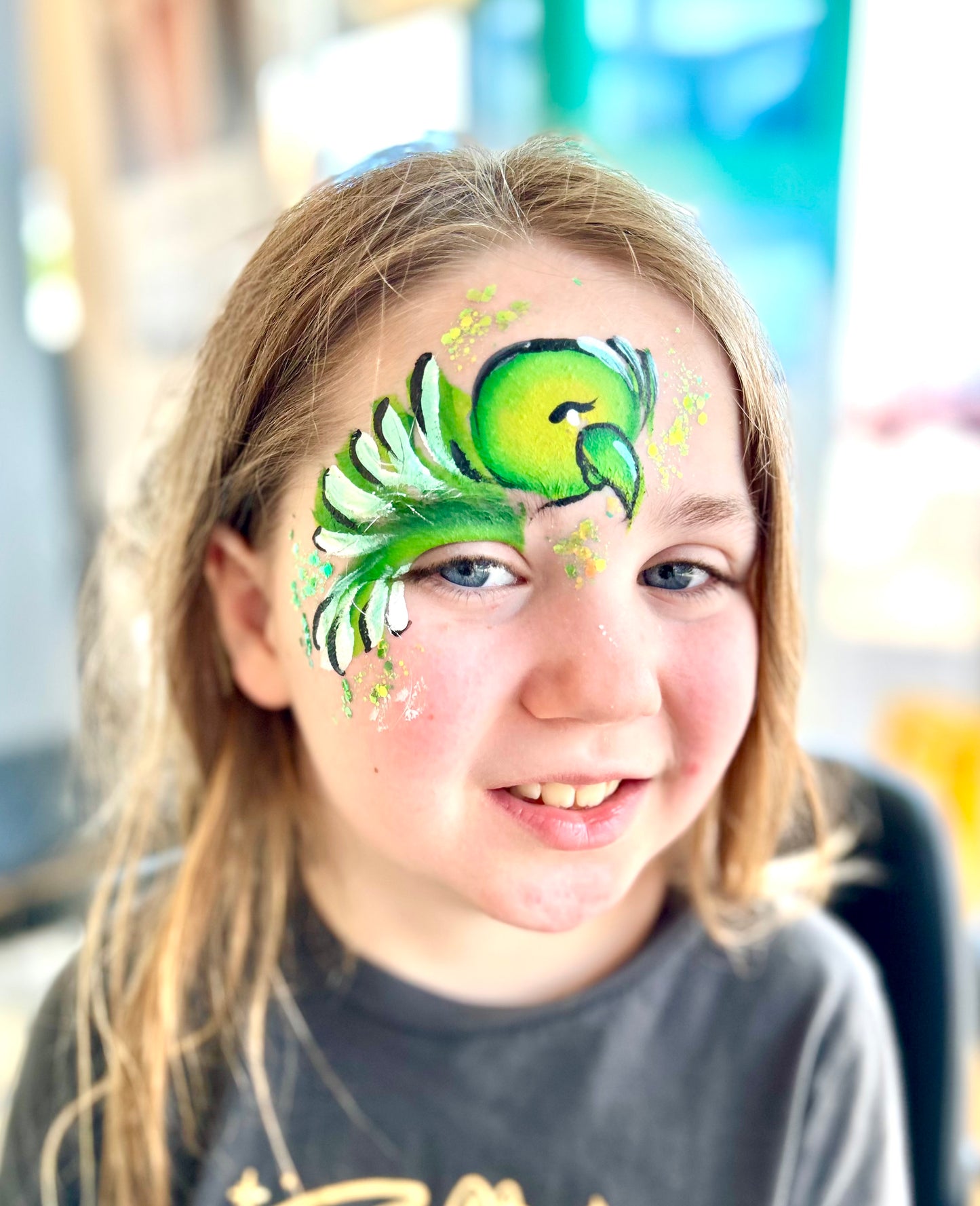 Young girl with a green and black face paint design of a peacock.